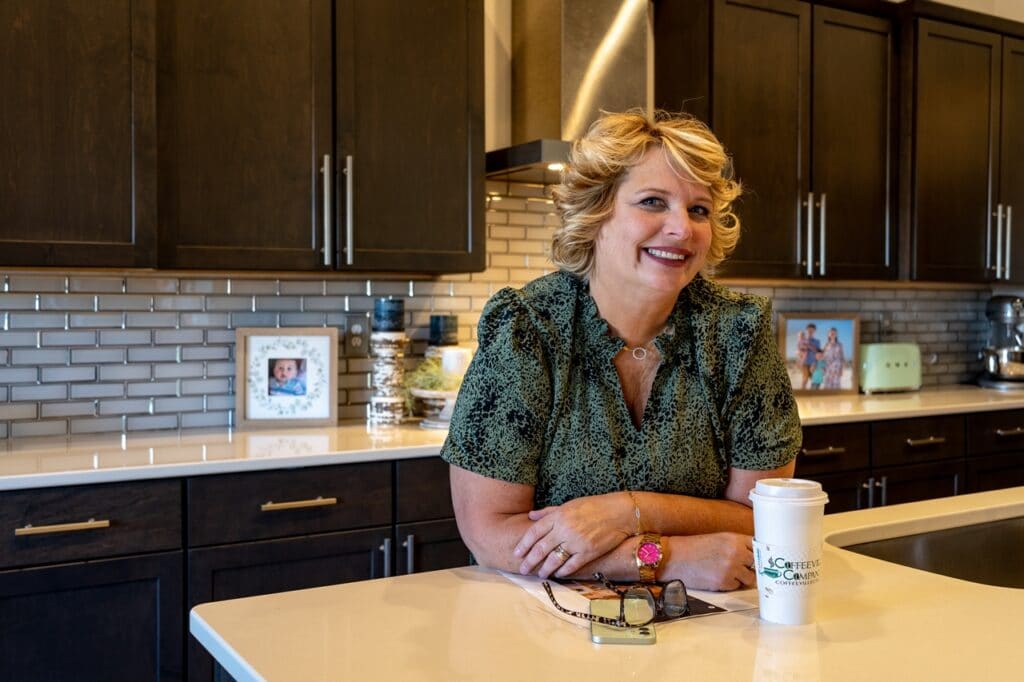 Wendy Wendorf smiling, leaning in her kitchen with coffee and glasses on the counter