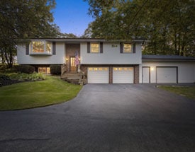 Night photo of stacked home with garage built into small hill, side storage, and large windows